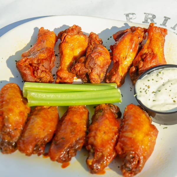 Ten glossy buffalo wings with celery sticks and a side of creamy ranch dip on a white plate.