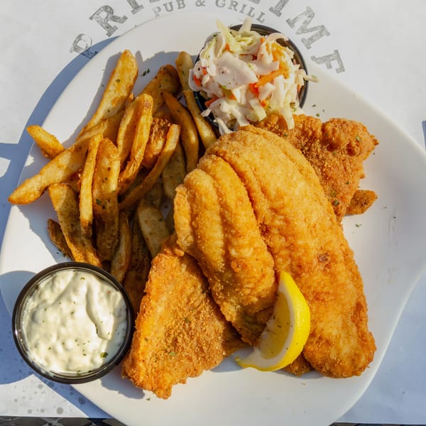 Golden-fried fish and chips with coleslaw, tartar sauce, and a lemon wedge on a white plate.