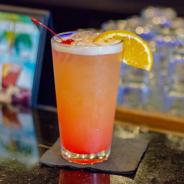 A vibrant orange and red cocktail with an orange slice and cherry on a bar counter.