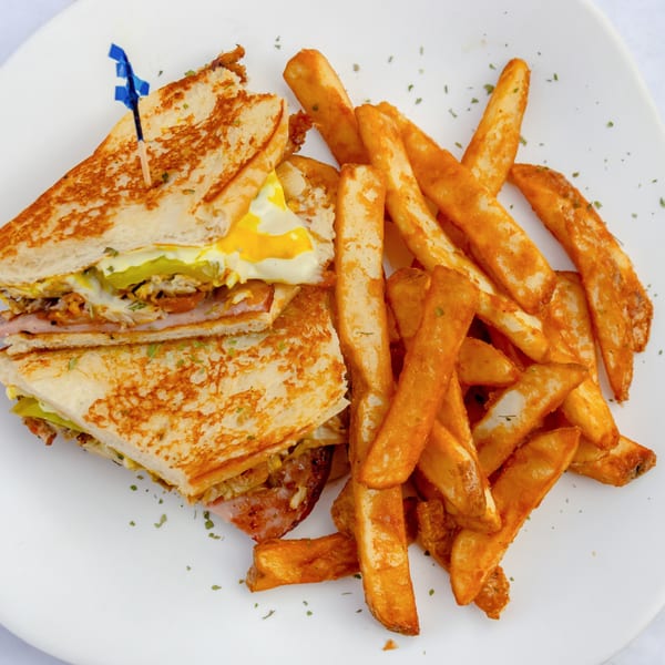 Grilled sandwich with egg, ham, and pickles, served with a side of golden french fries.
