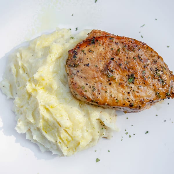 Grilled pork chop with herbs and spices, served alongside a generous portion of mashed potatoes.