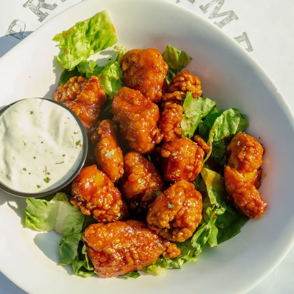 A white bowl filled with crispy orange chicken bites on a bed of lettuce, with a side of ranch.