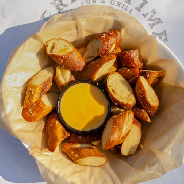 Golden pretzel bites with salt and cheese dip in a basket on a restaurant menu.