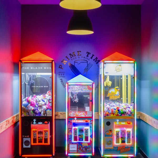 Three brightly lit arcade claw machines stand against a wall with the "Prime Time Pub & Grill" logo.