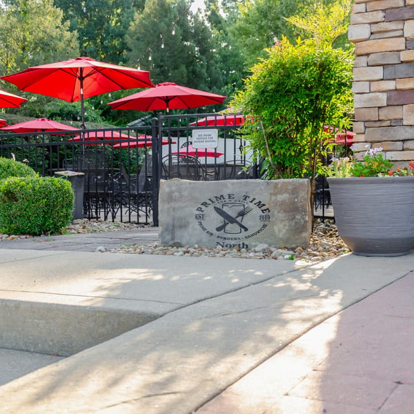 Prime Time Pub & Grill sign on a stone slab, with red umbrellas and outdoor seating in the background.