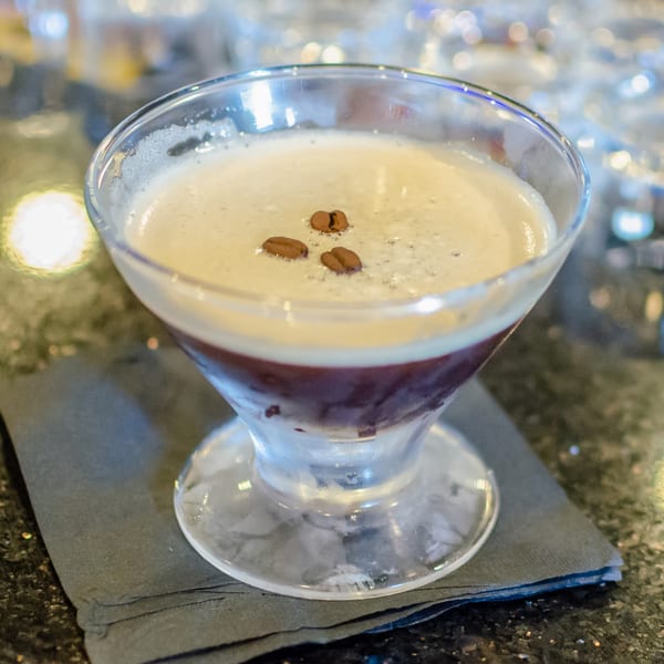 Espresso martini in a coupe glass, garnished with coffee beans, on a dark napkin.