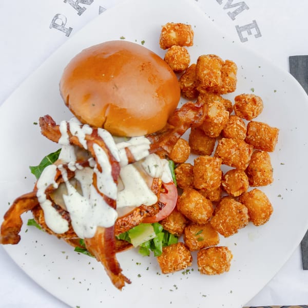 A chicken sandwich with bacon, lettuce, tomato, and ranch dressing, served with tater tots.
