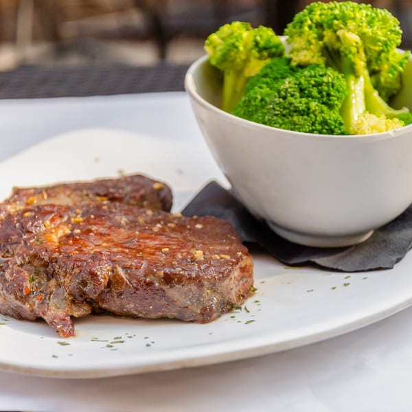 Grilled steak with herbs and a side of steamed broccoli in a white bowl on a white plate.